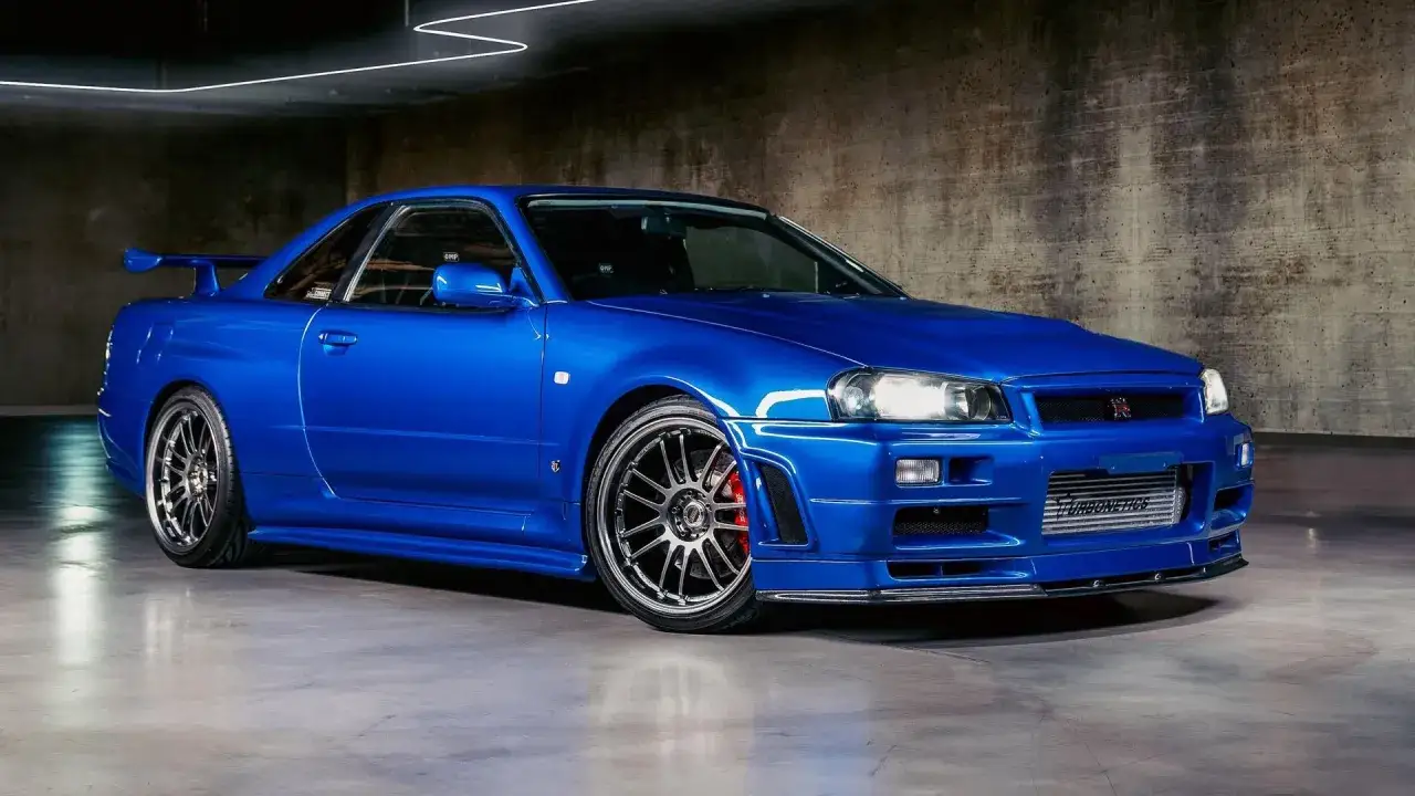 Błękitny Nissan GTR R34 z charakterystycznym spoilerem i felgami, gotowy do podboju dróg.