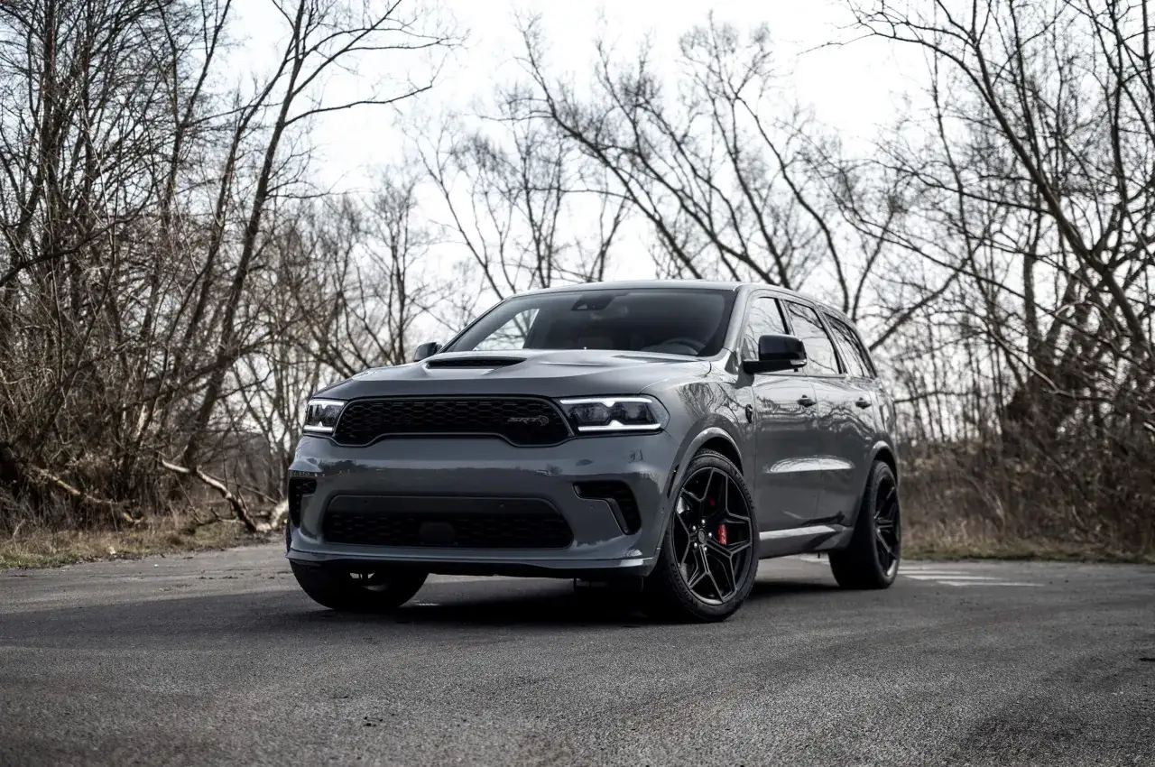 Szary Dodge Durango 5.7 Hemi SRT z czarnymi felgami stoi na pustej drodze, otoczony nagimi drzewami.