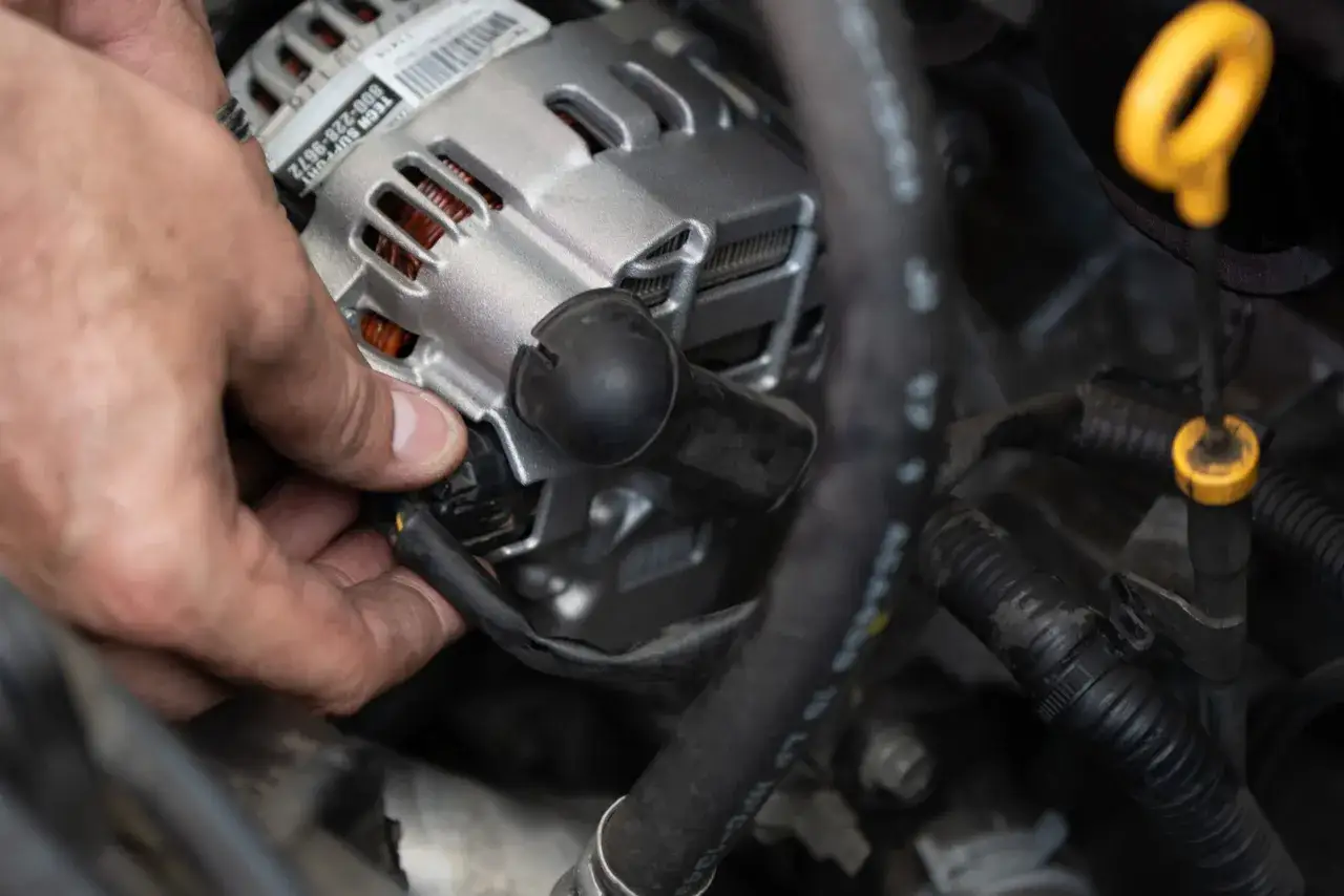 Dłoń mechanika podłącza nowy alternator. Zastanawiasz się, ile kosztuje wymiana alternatora?