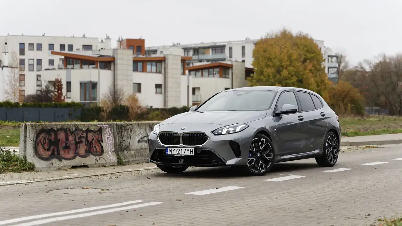 Szare BMW 120 na tle nowoczesnych budynków i betonowych barier z graffiti.