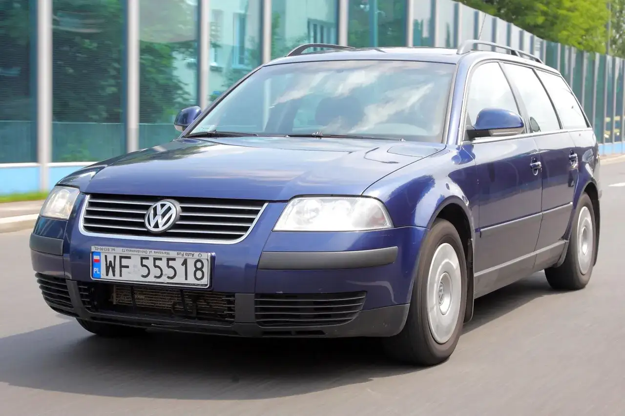 Granatowy Volkswagen Passat kombi, model b5, jedzie po drodze.