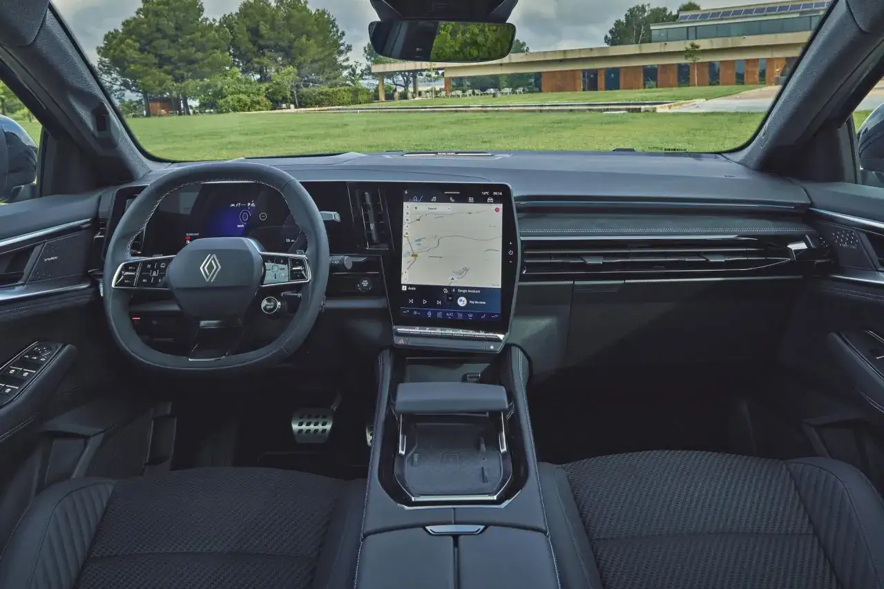 Wnętrze Renault Austral 2025 z dużym ekranem multimedialnym i cyfrowymi zegarami. Widok na zielony krajobraz przez przednią szybę.