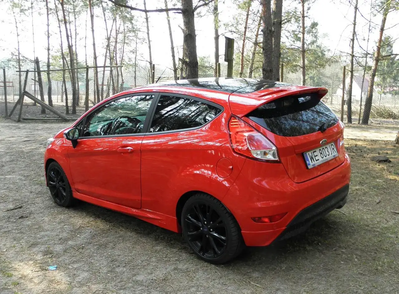 Czerwona Fiesta ST z czarnym dachem i felgami stoi na leśnej polanie.