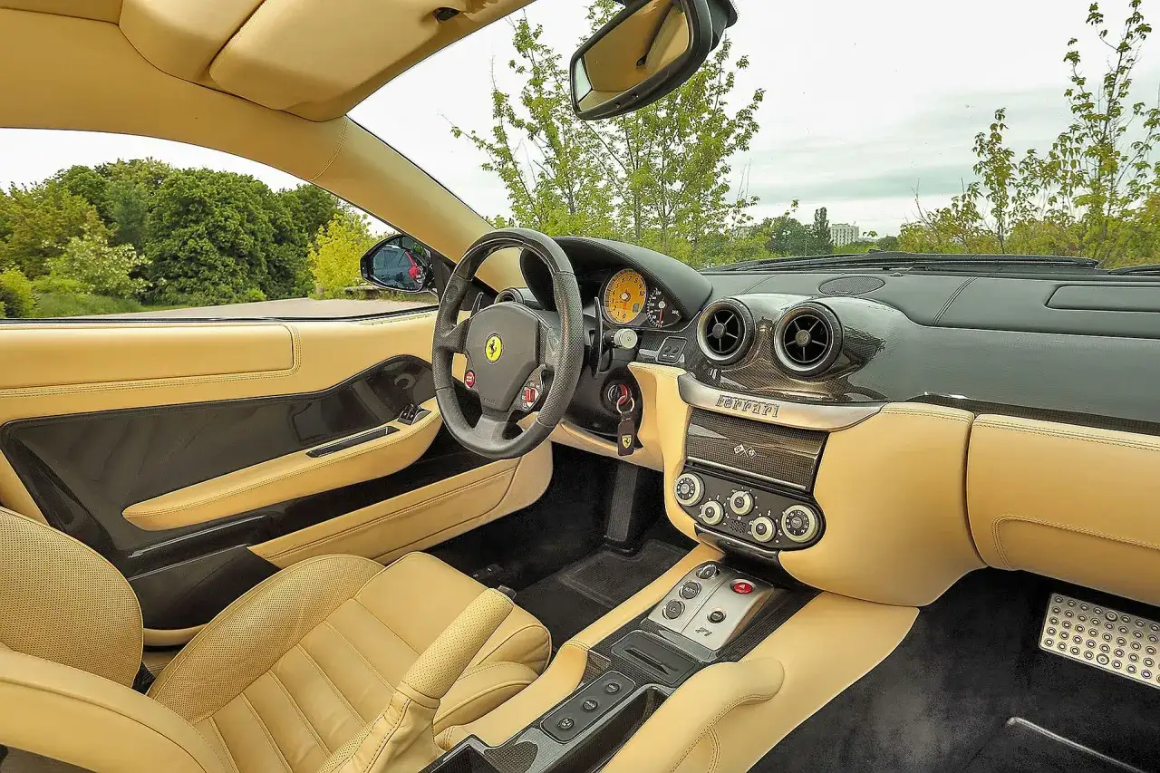 Wnętrze Ferrari 599: beżowa skórzana tapicerka, sportowa kierownica, panel z przyciskami i nawiewami.