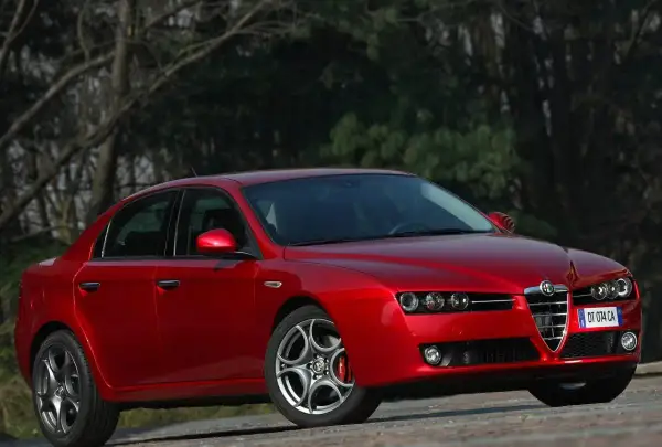 Czerwone Alfa Romeo 159 1.9 JTD z charakterystycznym grillem, zaparkowane na tle drzew.