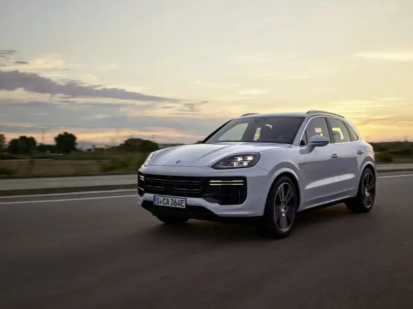 Biały Porsche Cayenne Turbo sunie po drodze o zachodzie słońca, z chmurami malującymi niebo.