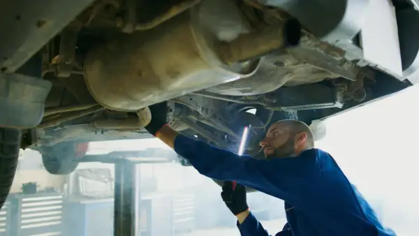 Mechanik w niebieskim kombinezonie oświetla latarką p0420 podwozie samochodu.