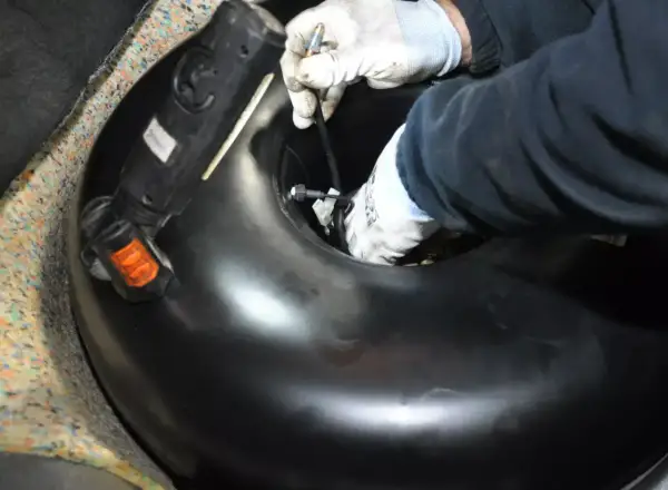 Ręce w rękawiczkach montują lub demontują okrągły zbiornik LPG w bagażniku samochodu.