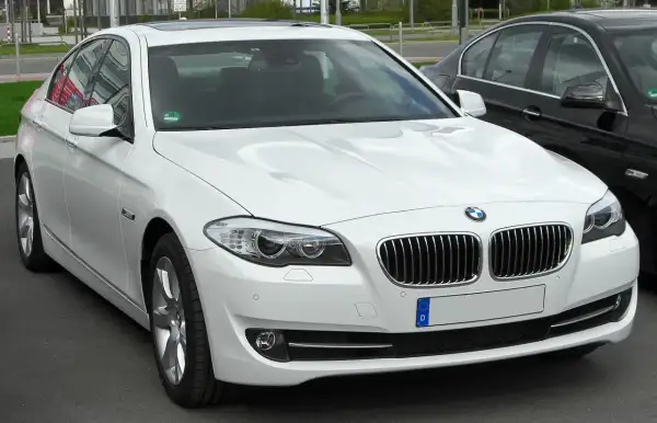 Białe BMW 535d z chromowanymi detalami i przyciemnianymi szybami, zaparkowane obok czarnego samochodu.