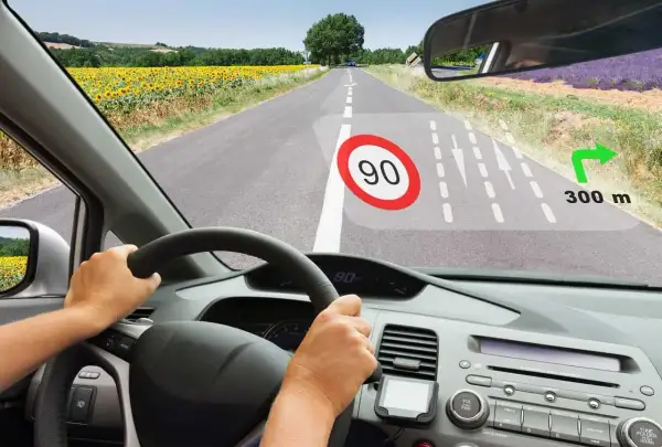 Widok z kabiny samochodu. Na szybie wyświetla się HUD z ograniczeniem prędkości 90, nawigacją i odległością 300 m do skrętu.