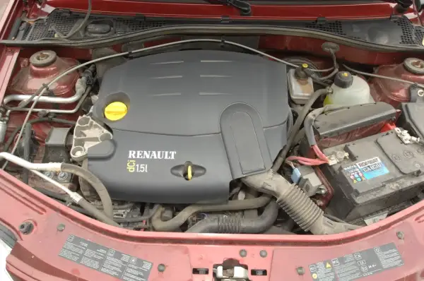Silnik Renault 1.5 dCi w samochodzie Dacia. Widoczny jest czarny plastikowy dekiel silnika z napisem RENAULT 1.5 dCi, akumulator i elementy układu chłodzenia.