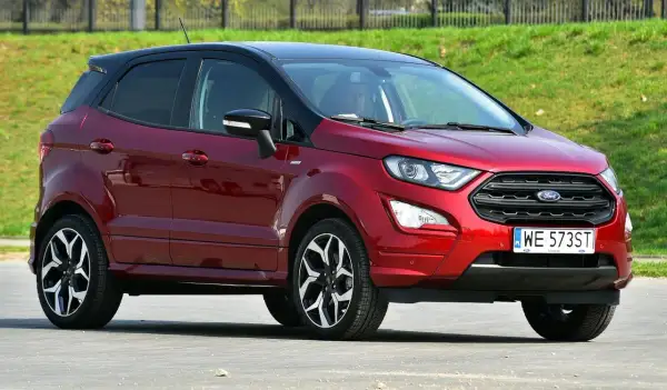 Czerwony Ford EcoSport z czarnym dachem, zaparkowany na tle zielonego zbocza.
